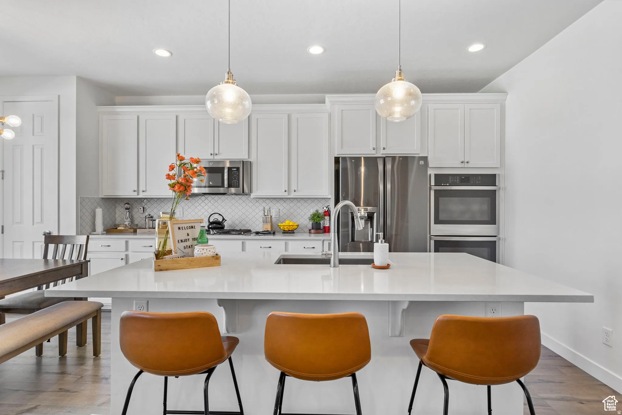 Kitchen with white cabinets, stainless steel appliances, a kitchen island with sink, and hanging light fixtures