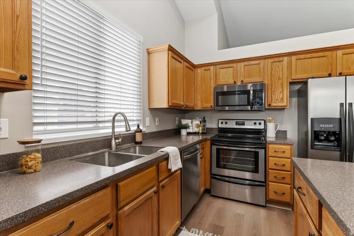 Kitchen with stainless steel appliances, light wood-style floors, wood finish cabinets, and dark stone counters