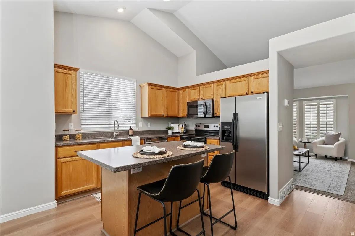 Kitchen with stainless steel appliances, a kitchen island, dark countertops, a breakfast bar, and light wood-style floors