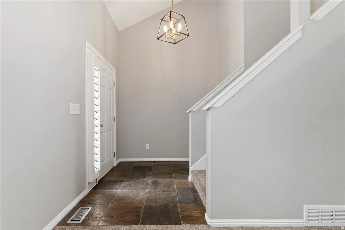 Foyer entrance featuring dark stone finish flooring, lofted ceiling, and hanging lights