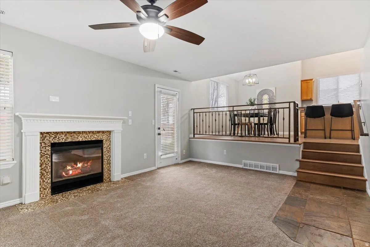 Unfurnished living room with dark colored carpet, a fireplace, and a ceiling fan