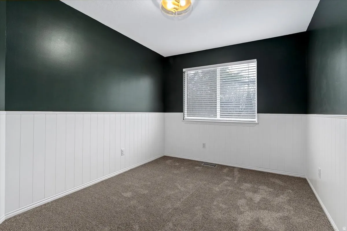 Unfurnished room featuring dark colored carpet and wainscoting