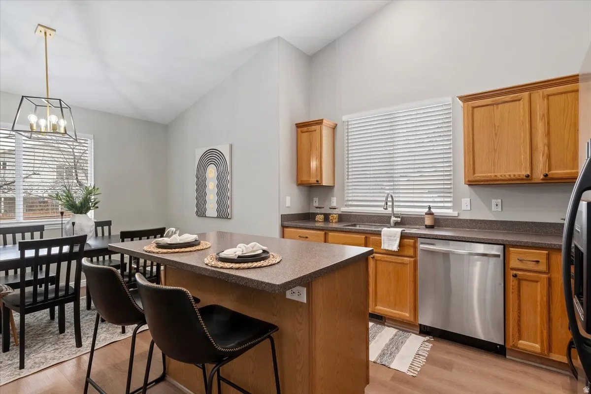 Kitchen featuring dark countertops, vaulted ceiling, a breakfast bar, dishwasher, and light wood finished floors