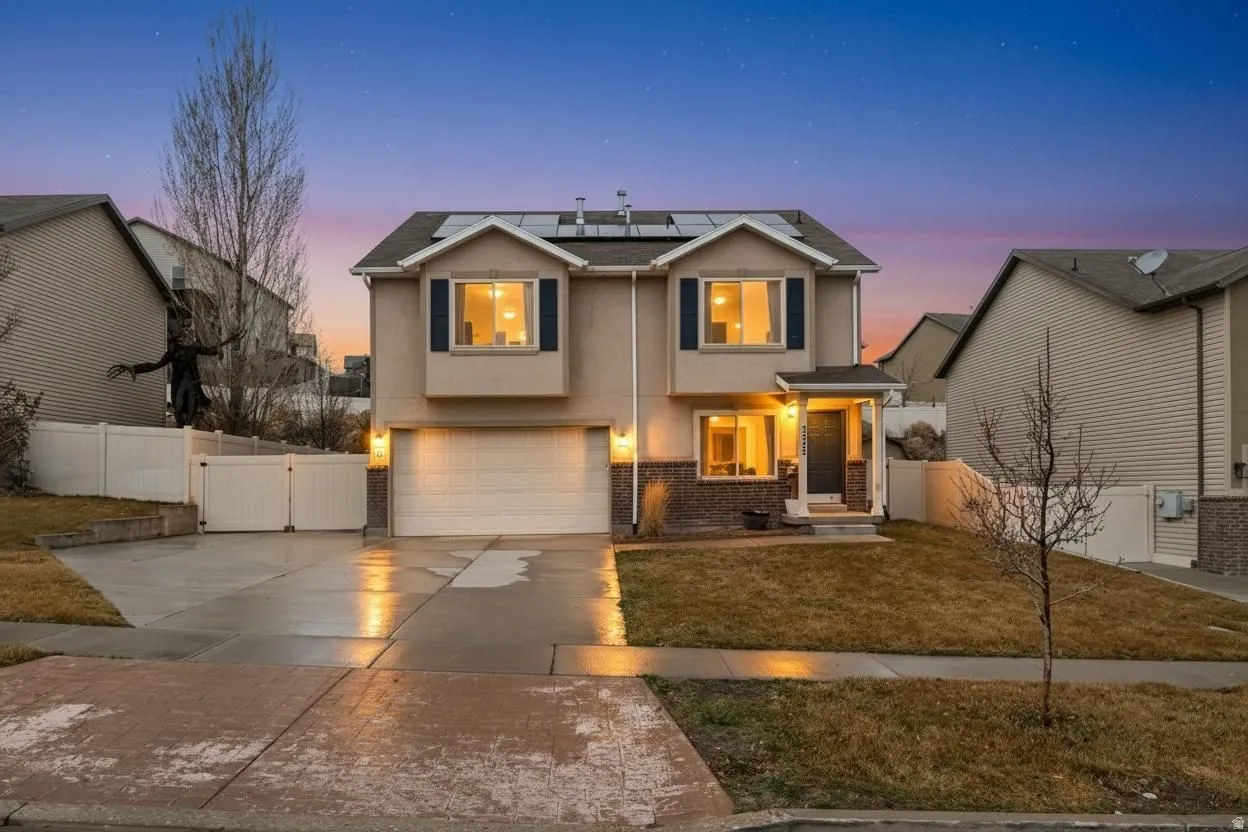 Traditional-style house with roof mounted solar panels, a gate, stucco siding, an attached garage, and concrete driveway