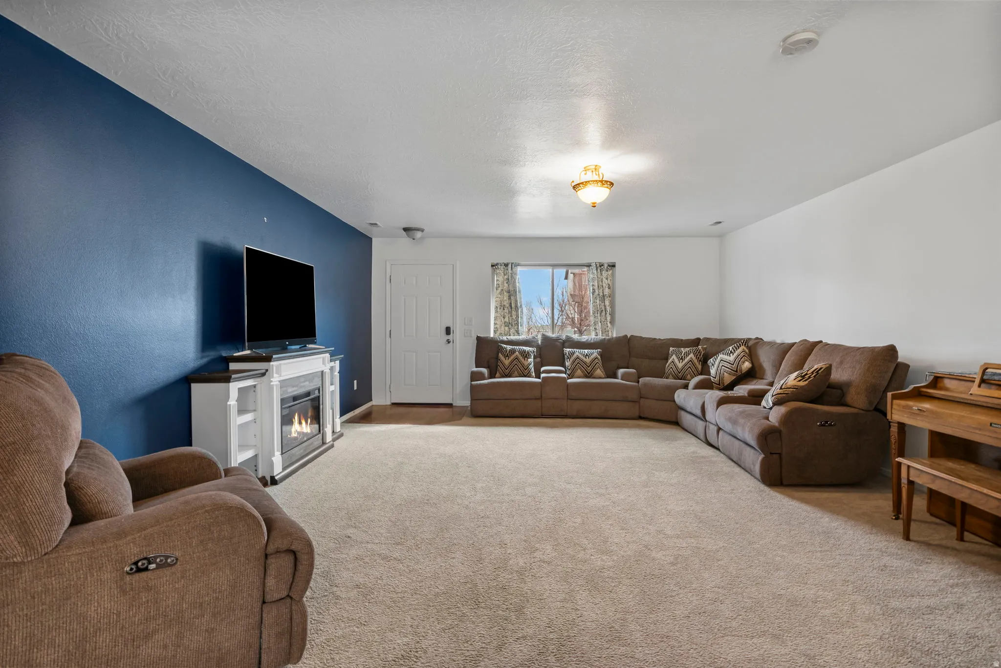 Living room featuring light colored carpet, a glass covered fireplace, and a textured ceiling