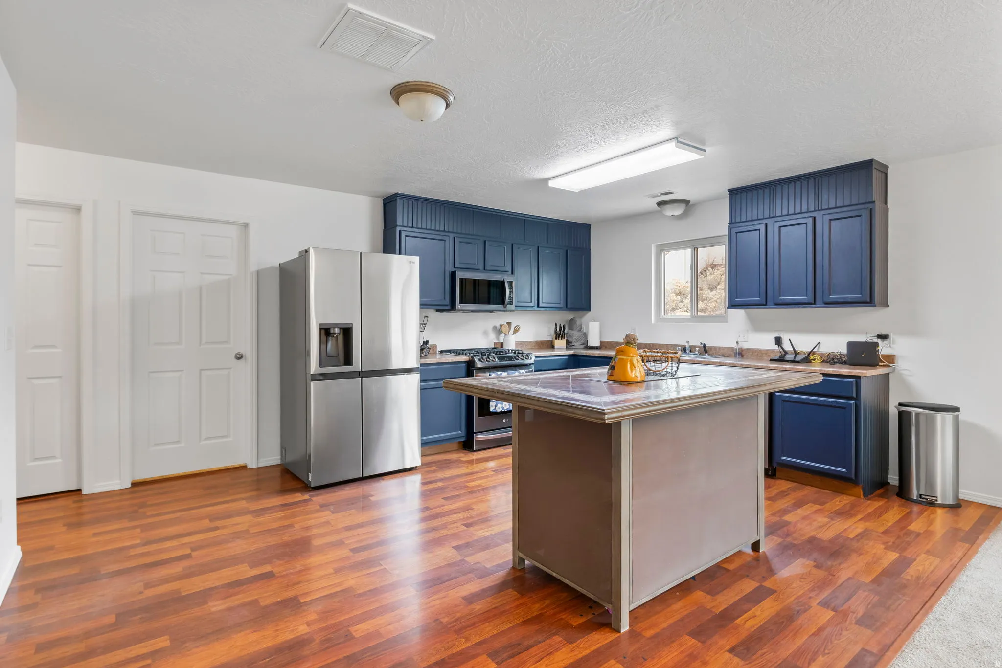 Kitchen with blue cabinetry, stainless steel appliances, a center island, dark wood-style floors, and a textured ceiling