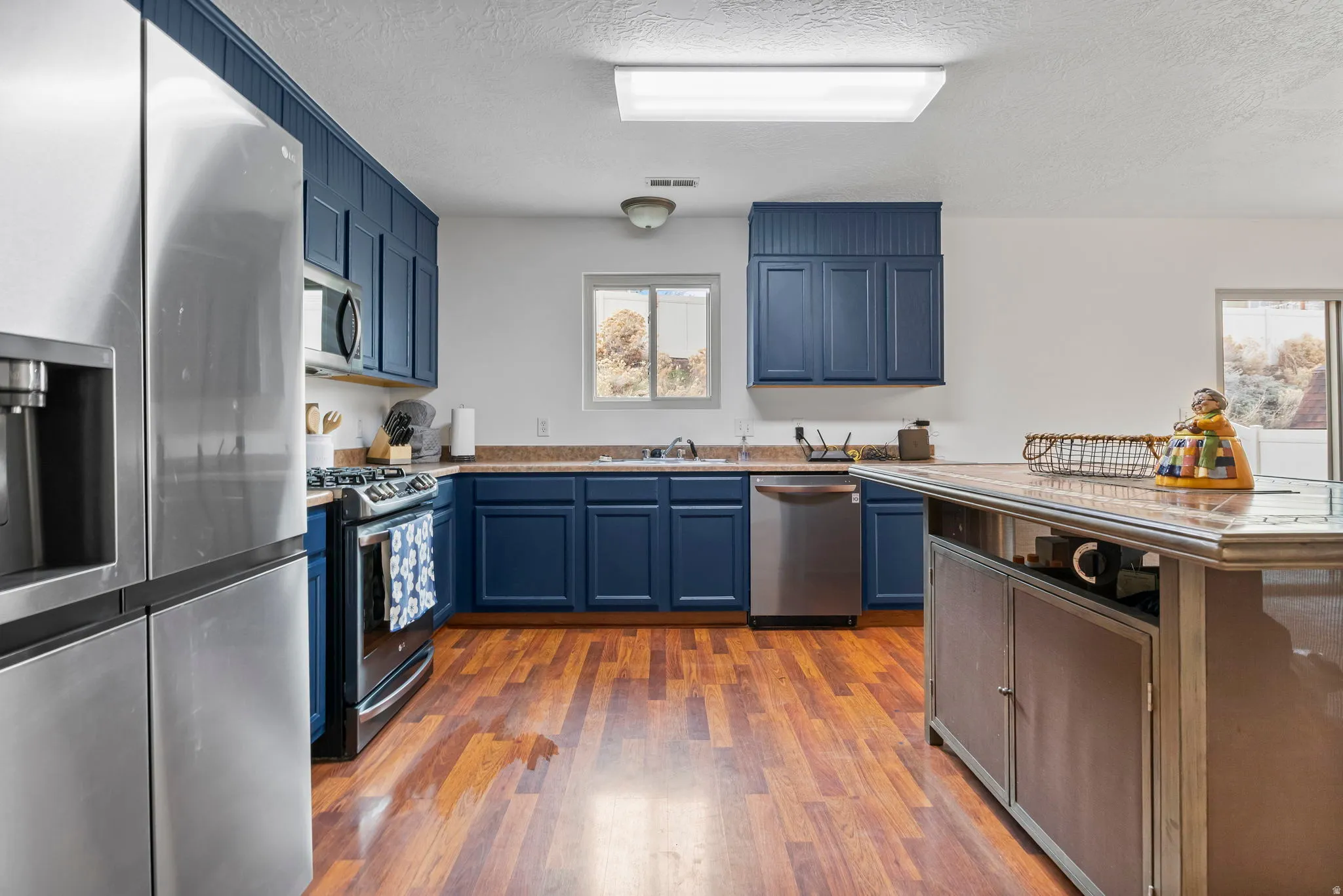 Kitchen featuring stainless steel appliances, blue cabinetry, a textured ceiling, and light countertops