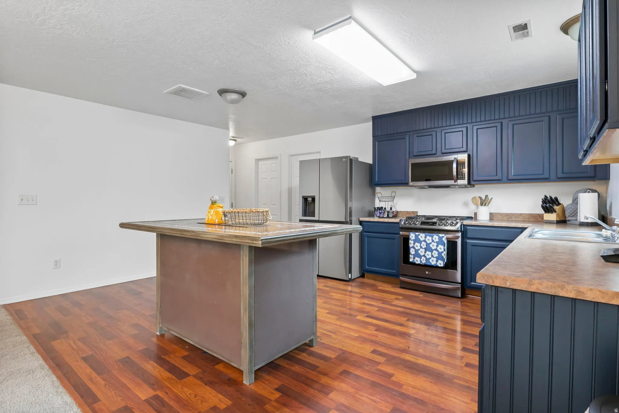 Kitchen featuring a kitchen island, stainless steel appliances, light countertops, a textured ceiling, and dark wood-type flooring