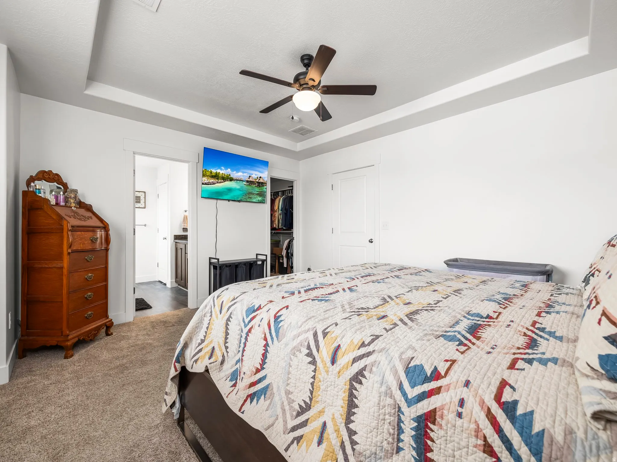 Carpeted bedroom featuring a raised ceiling, a ceiling fan, and a spacious closet