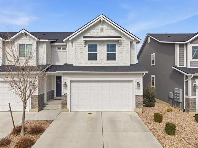 View of front of home with stone siding, driveway, an attached garage, and roof with shingles