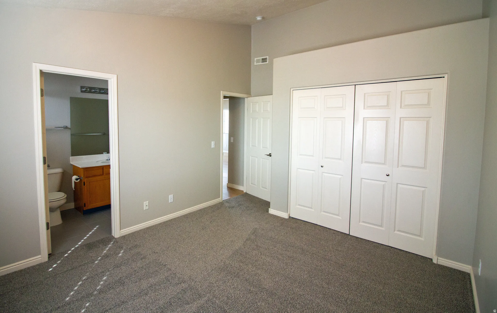 Unfurnished bedroom with dark carpet, a closet, and connected bathroom