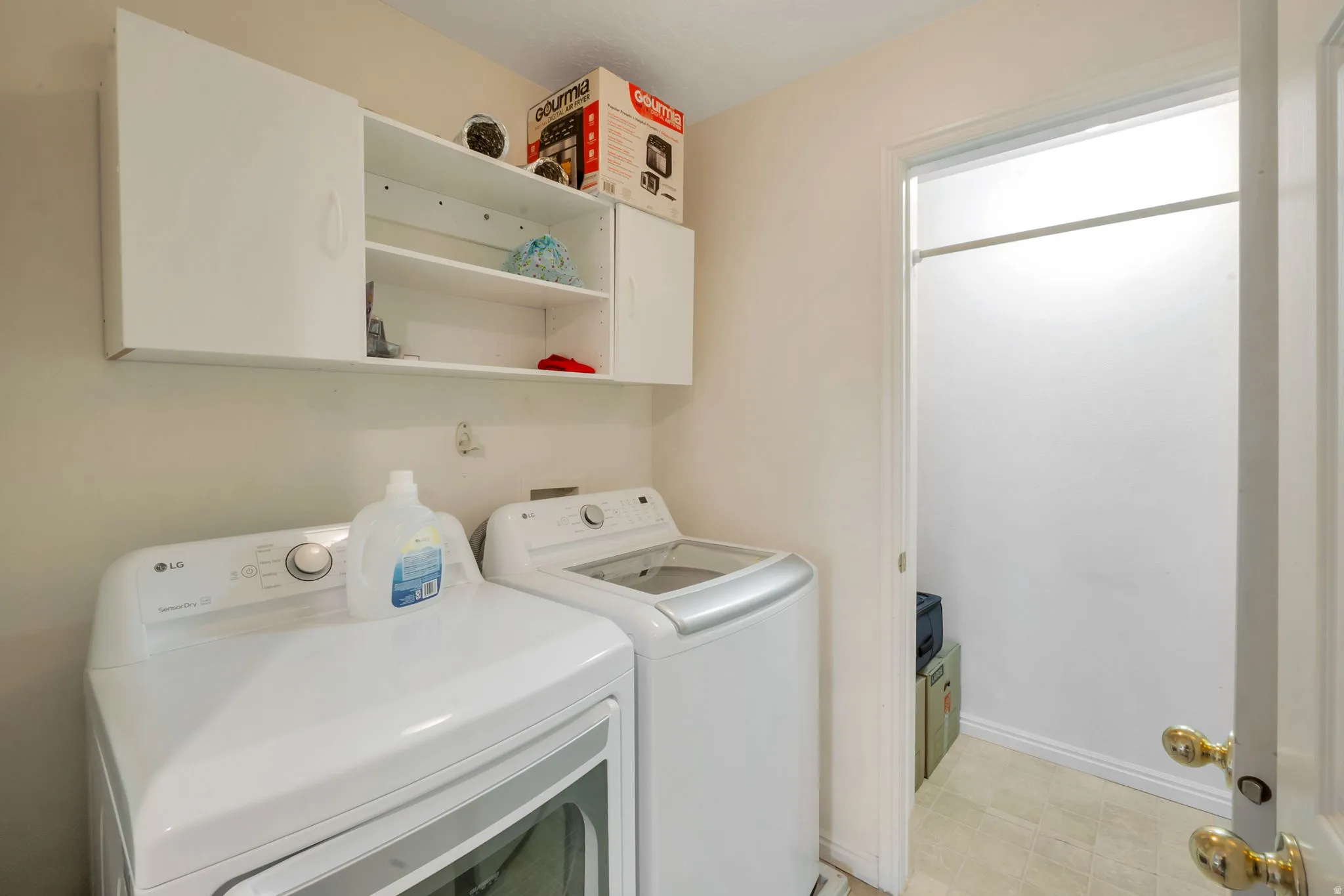 Laundry area featuring white wall cabinetry with open shelving, light-toned wall paint, and tiled flooring