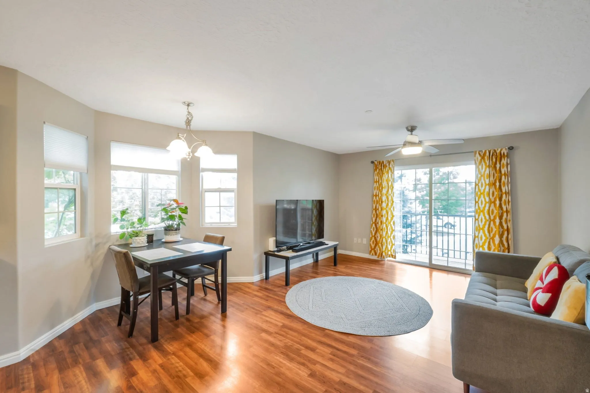 Open-concept living space featuring wood-finish flooring, a dining area with multiple windows, and a sliding glass door to a balcony