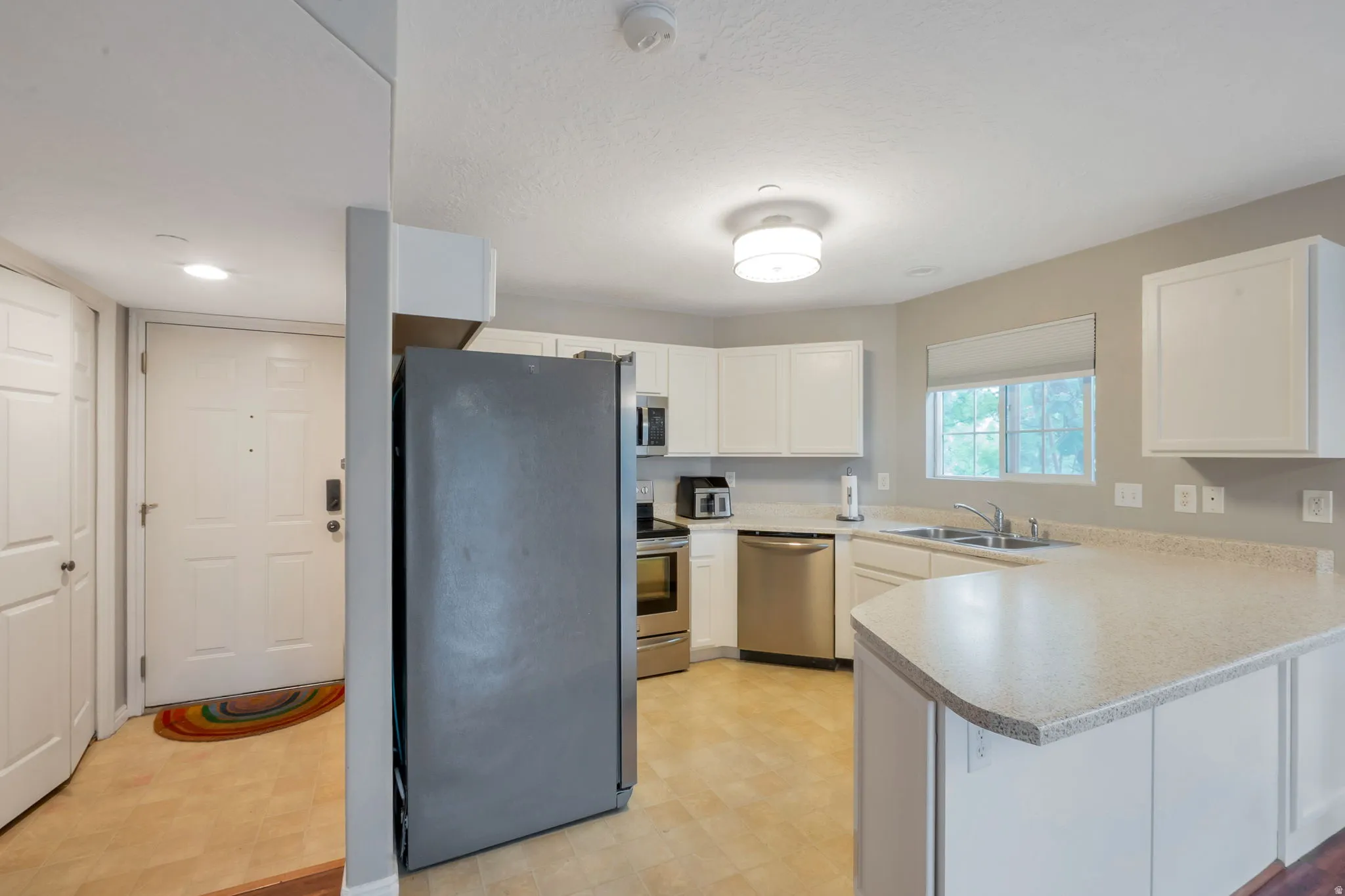 Kitchen featuring white cabinetry, light-toned countertops, a stainless steel dishwasher, a double basin sink, and wood-finish flooring