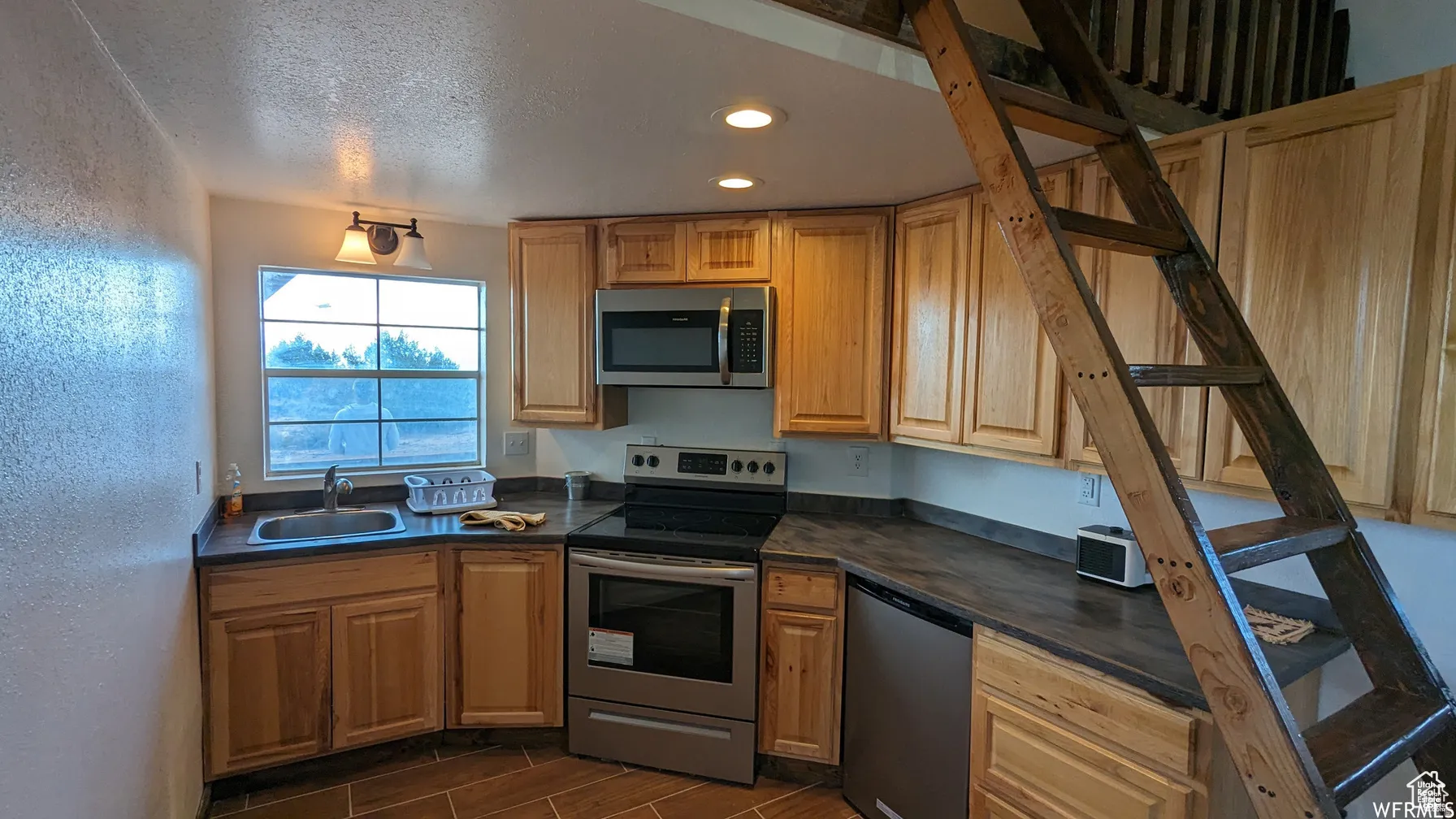 Kitchen with stainless steel appliances, dark countertops, a textured wall, recessed lighting, and wood finish floors
