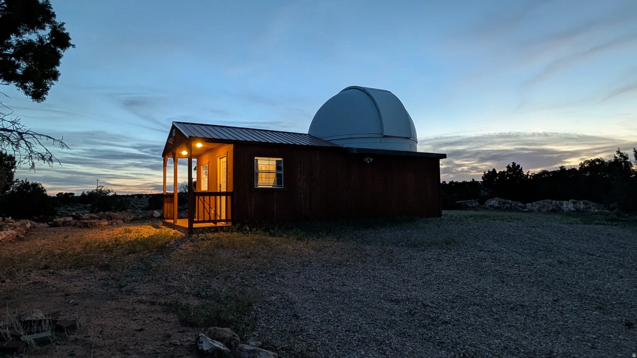 Observatory dome atop a structure with a wood-paneled exterior, metal roof, and covered front porch