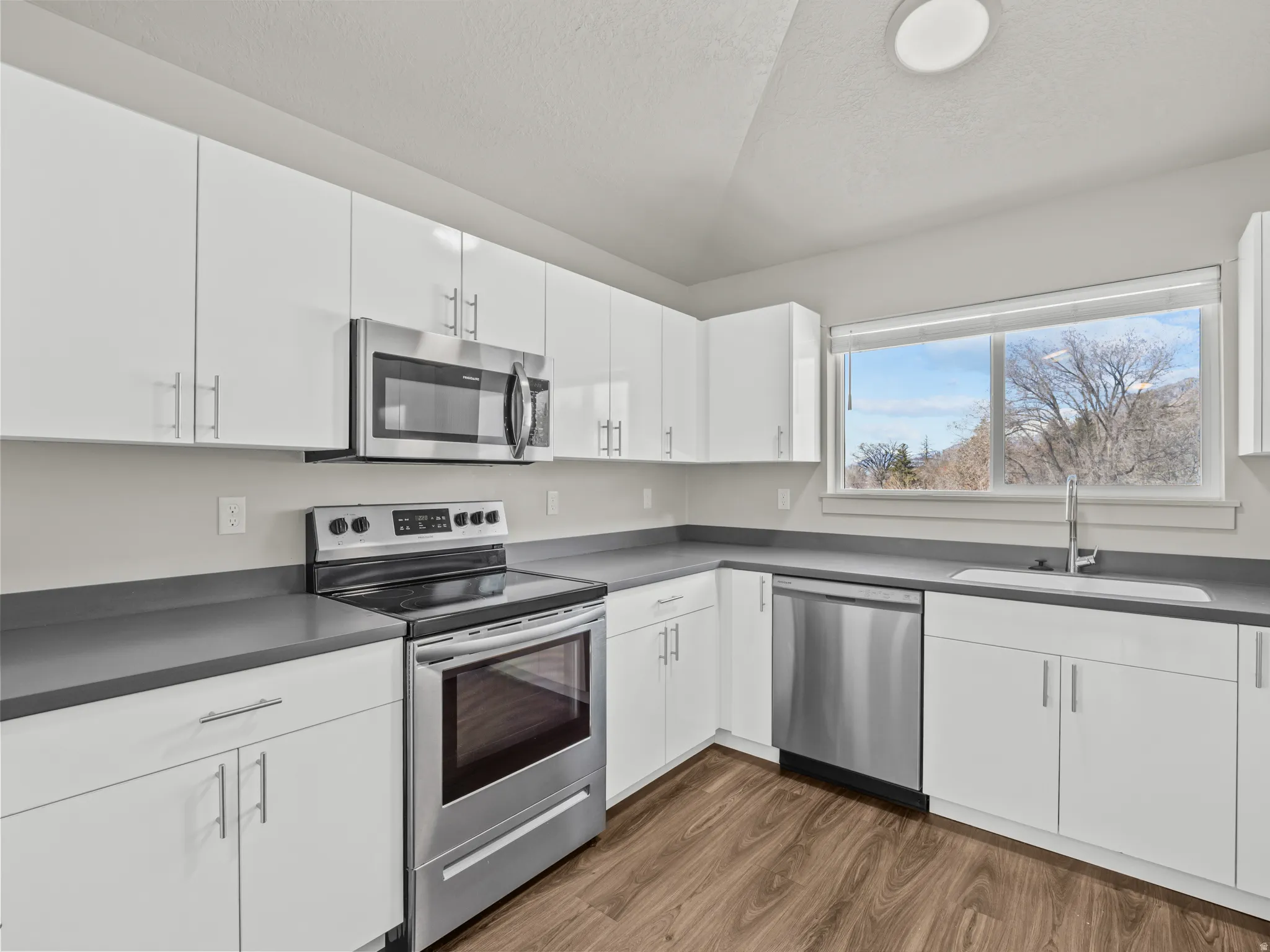 Kitchen with stainless steel appliances, white cabinetry, dark countertops, a textured ceiling, and dark wood-type flooring