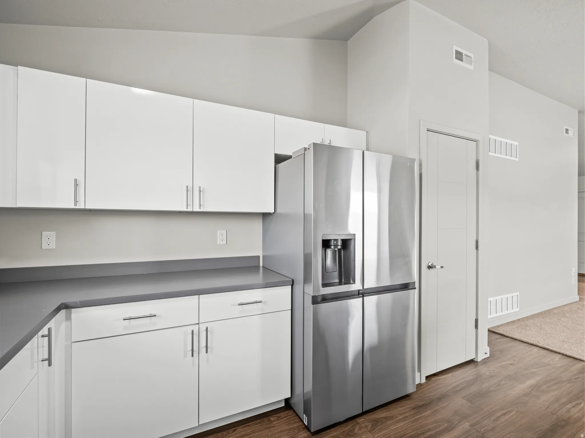 Kitchen with stainless steel fridge with ice dispenser, white cabinets, dark wood-style flooring, and dark countertops