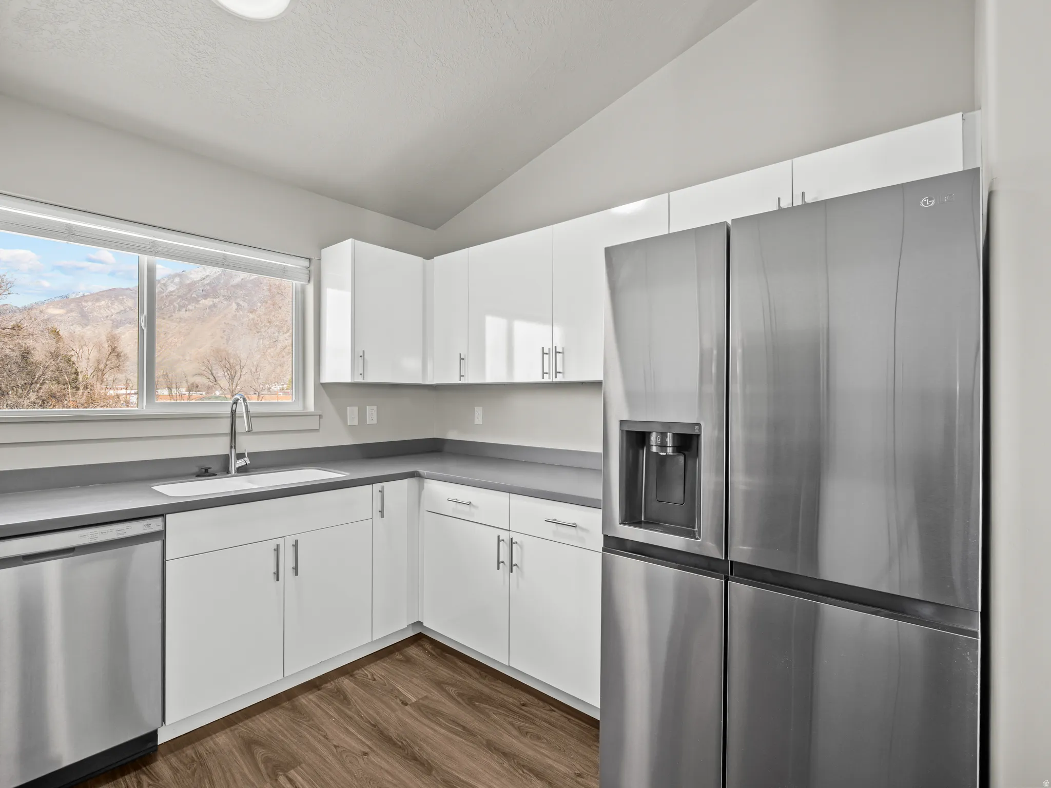 Kitchen featuring stainless steel appliances, white cabinetry, lofted ceiling, dark wood-style flooring, and a mountain view
