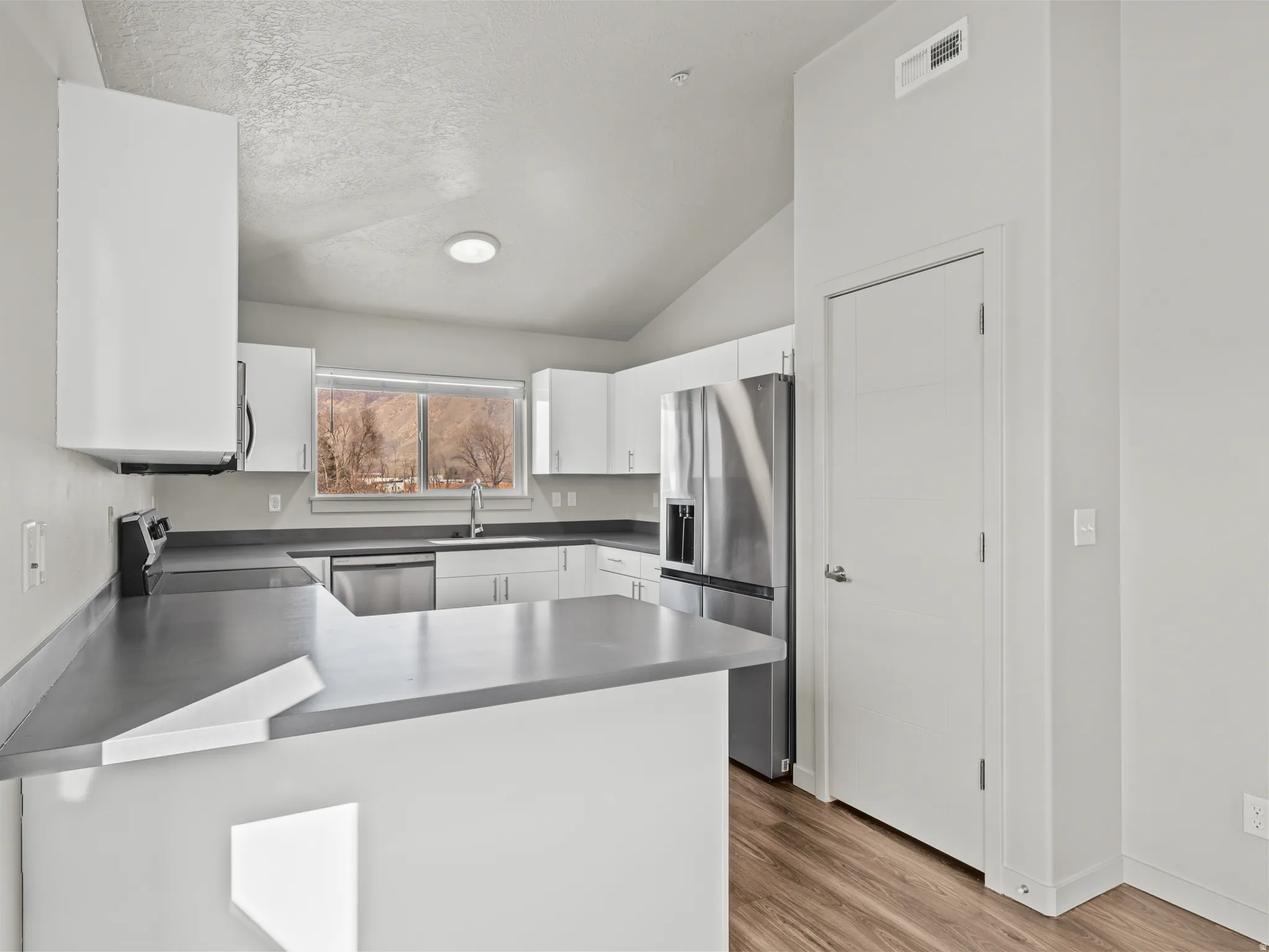 Kitchen featuring white cabinets, stainless steel appliances, a peninsula, light wood-style floors, and dark countertops