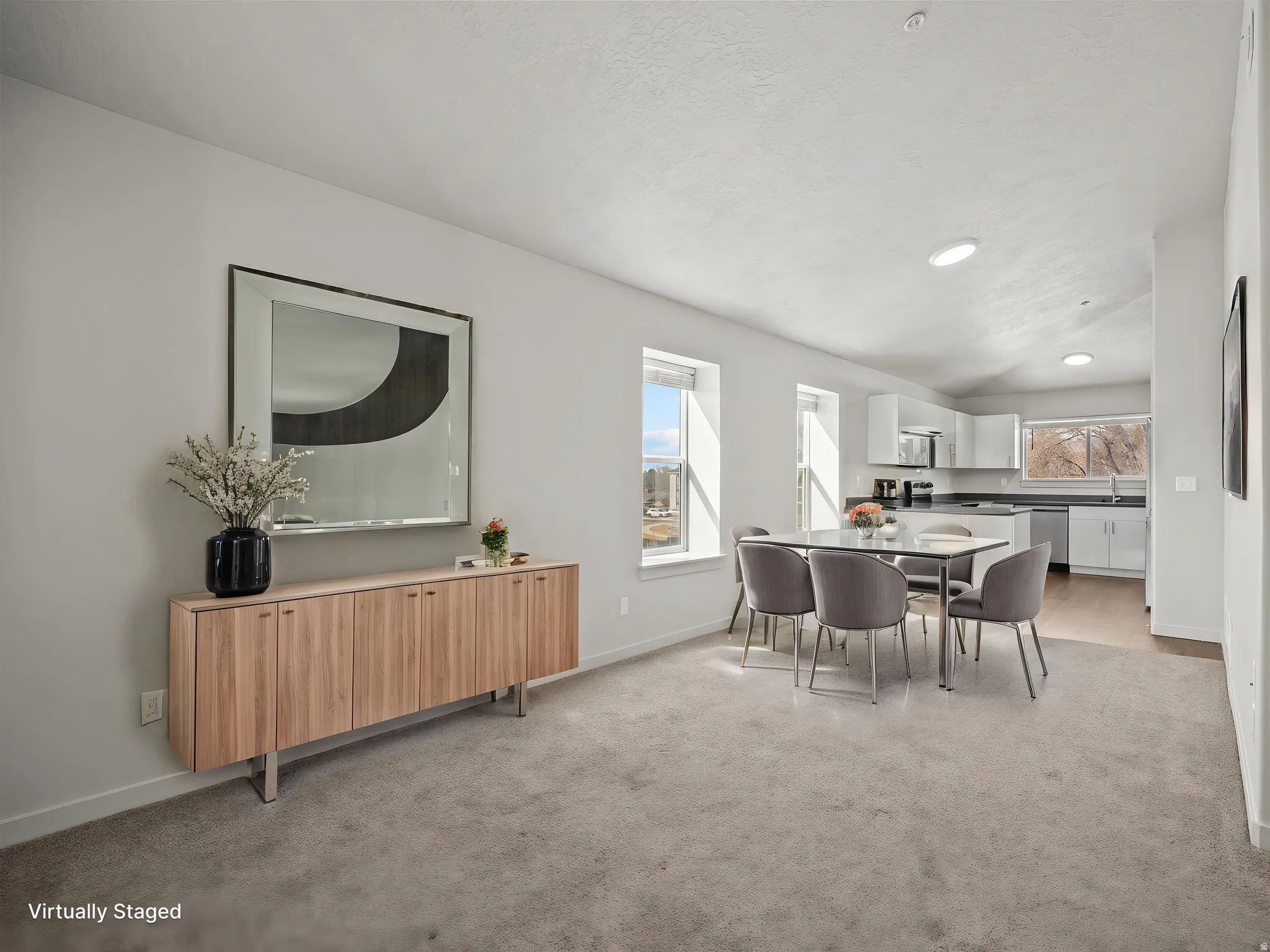 Open-concept living space featuring light gray carpeting, recessed lighting, and multiple windows providing natural light