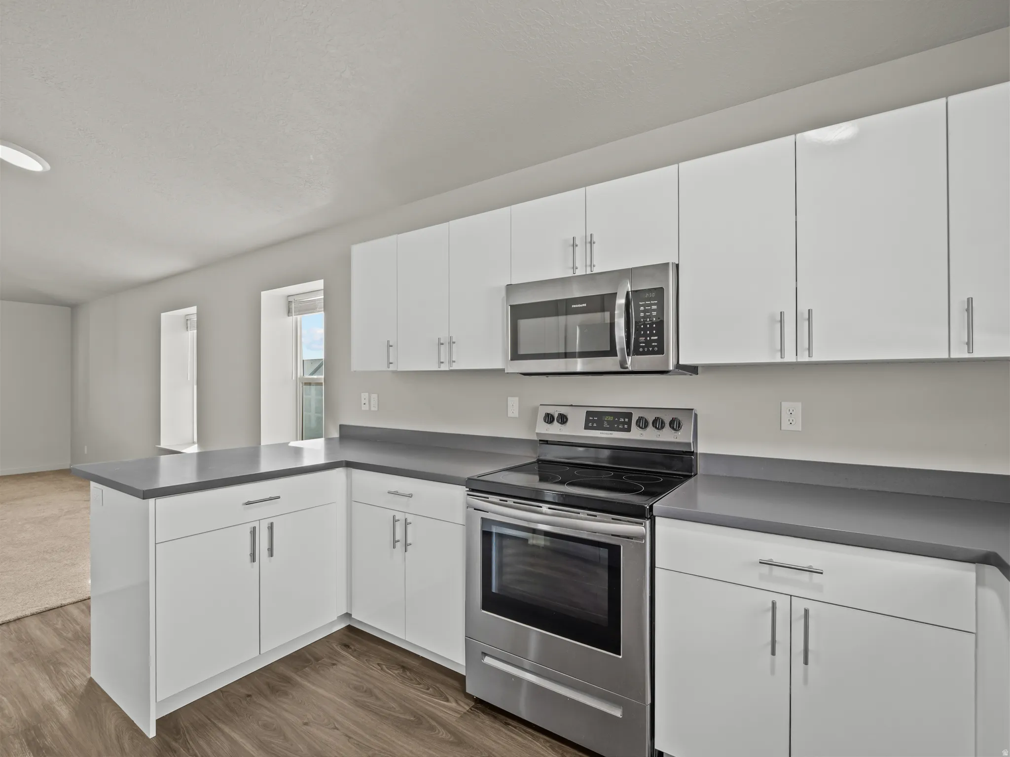 Kitchen featuring stainless steel appliances, white cabinetry, a peninsula, dark countertops, and a textured ceiling