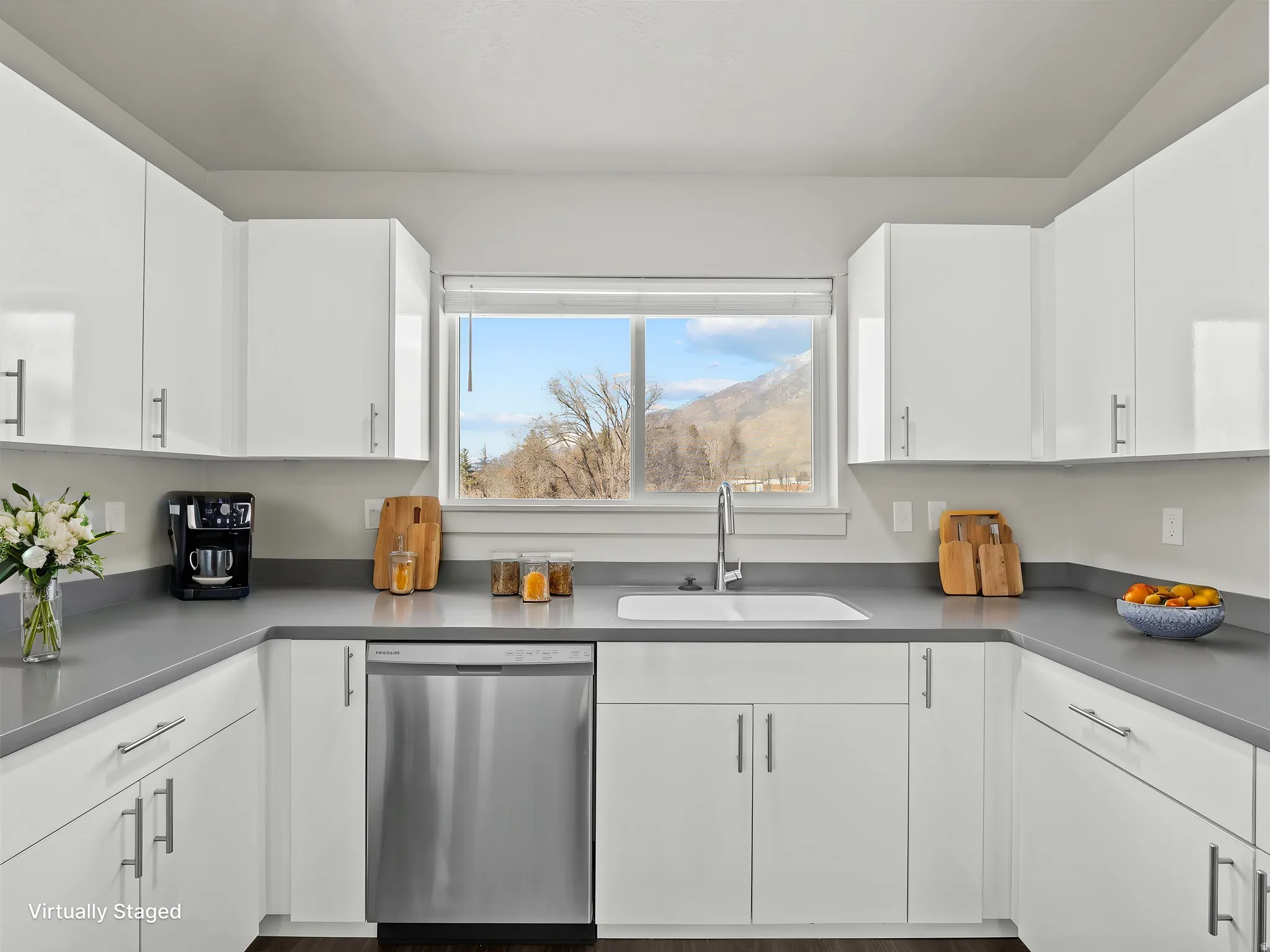 Modern kitchen featuring extensive white cabinetry with stainless steel pulls, light gray countertops, and a stainless steel dishwasher