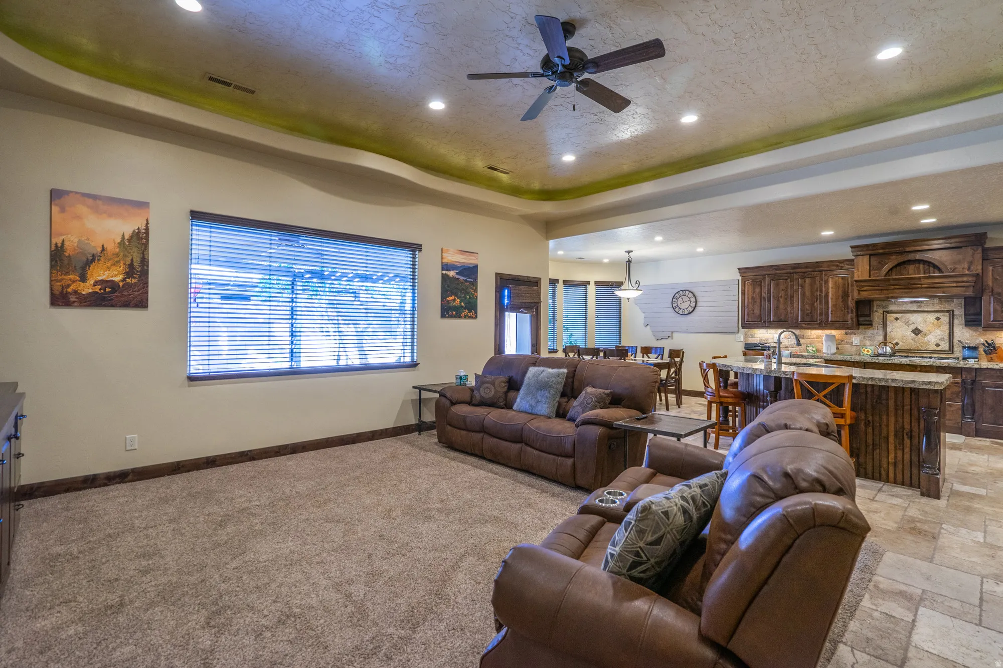Living area featuring a tray ceiling, a ceiling fan, stone tile flooring, and recessed lighting