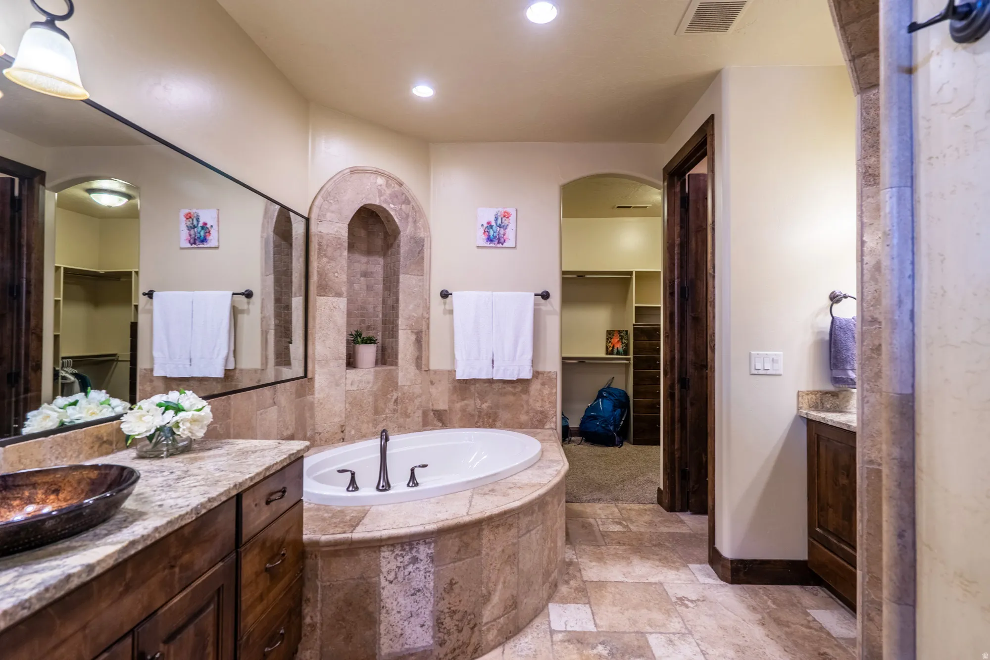 Full bath featuring a walk in closet, stone tile floors, two vanities, a garden tub, and recessed lighting