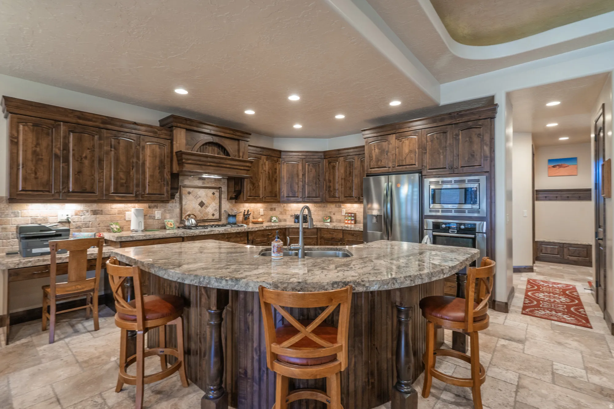 Kitchen with stone tile floors, dark wood finish cabinets, stainless steel appliances, a kitchen breakfast bar, and tasteful backsplash
