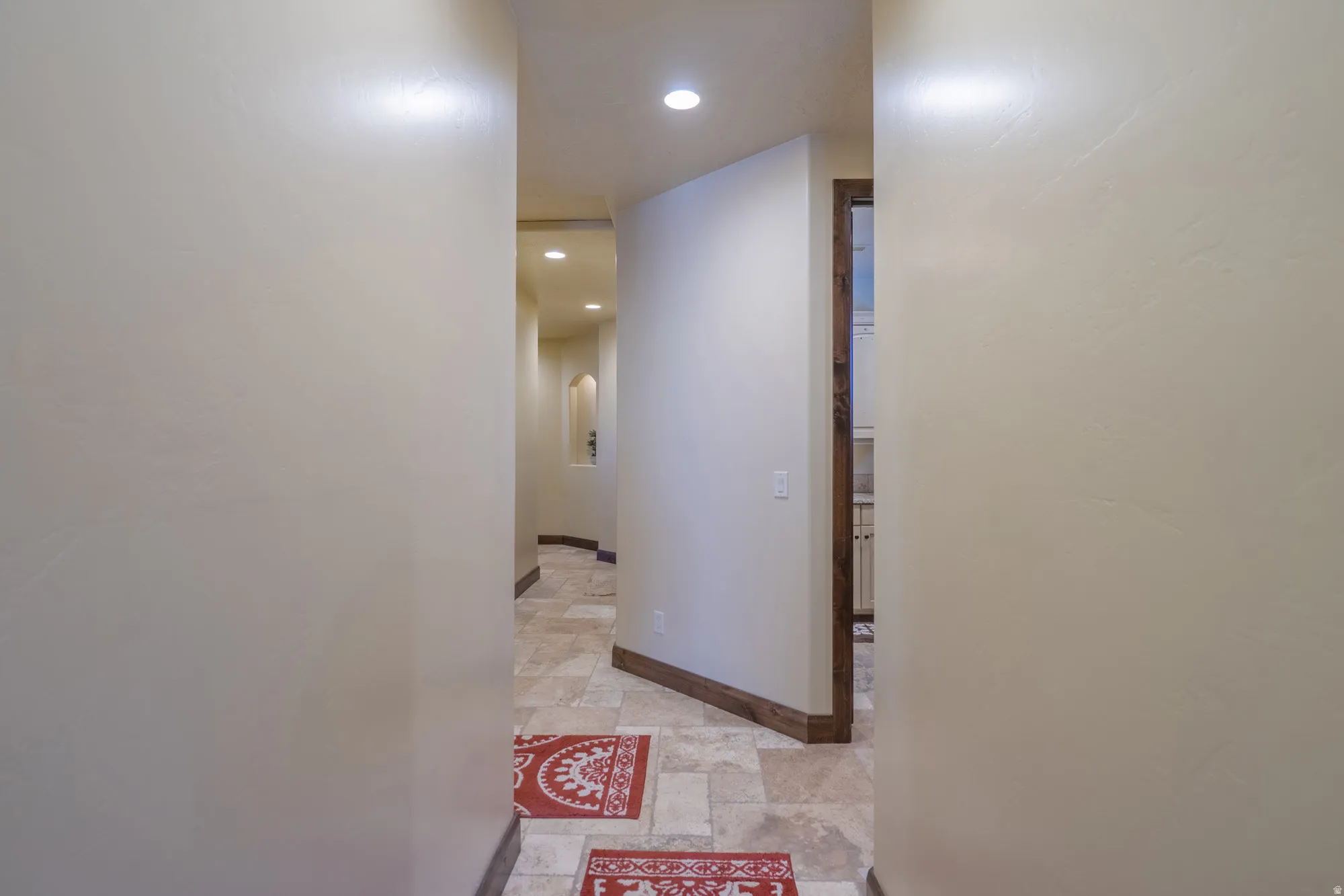 Hallway with recessed lighting, light stone finish floors, and arched walkways