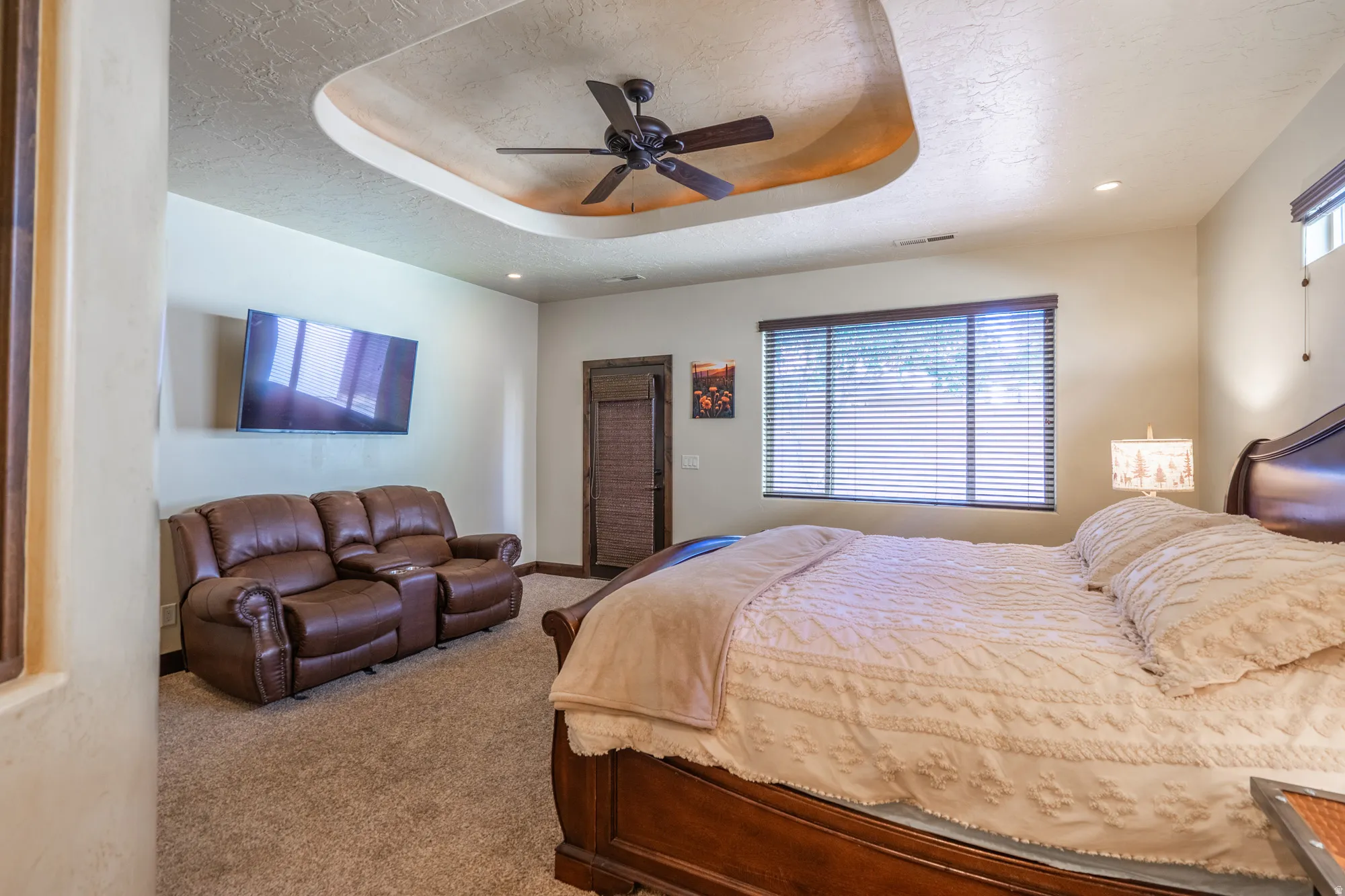 Bedroom featuring a ceiling fan, a tray ceiling, carpet, multiple windows, and a textured ceiling