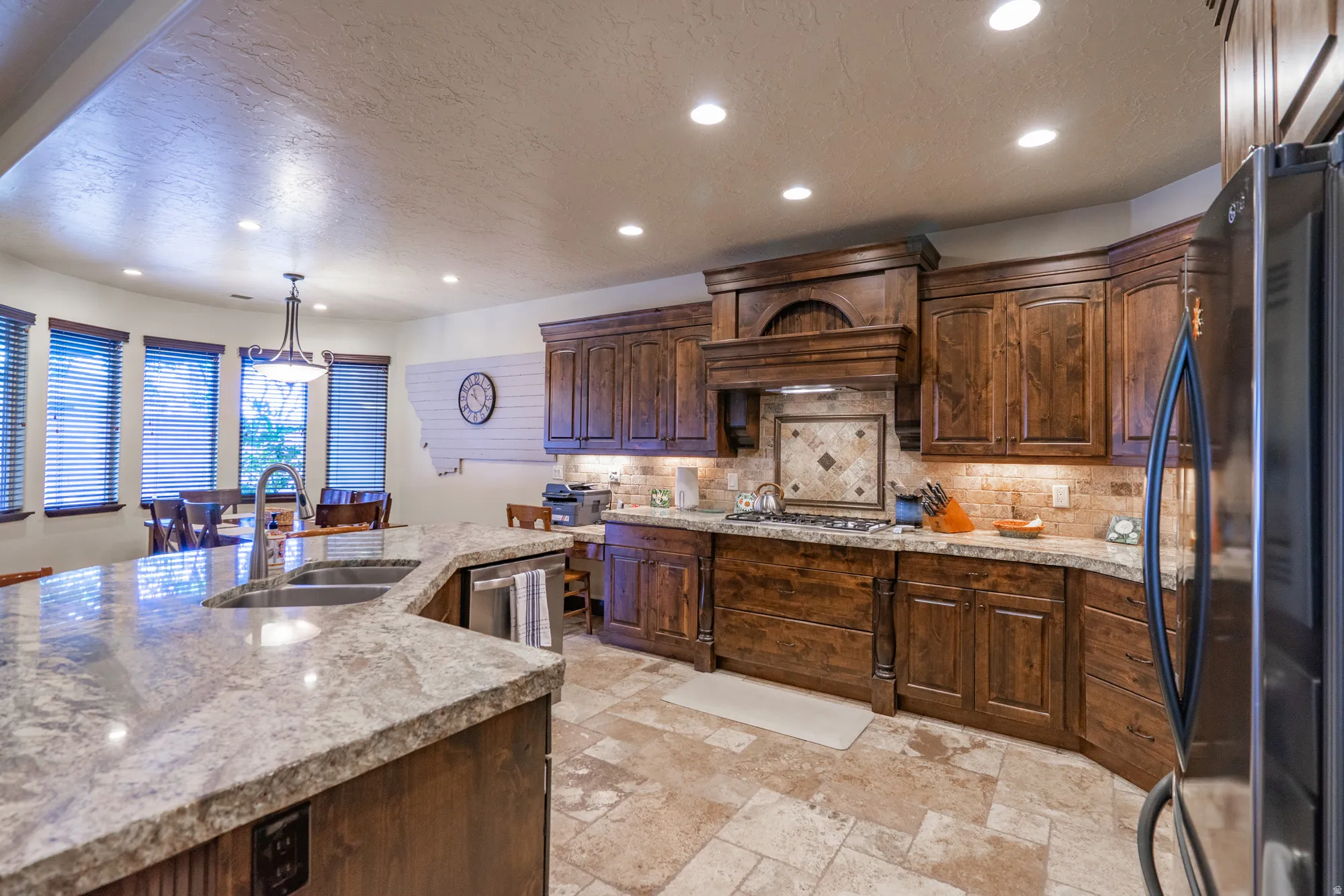 Kitchen featuring stainless steel appliances, a textured ceiling, hanging light fixtures, dark wood finish cabinetry, and tasteful backsplash