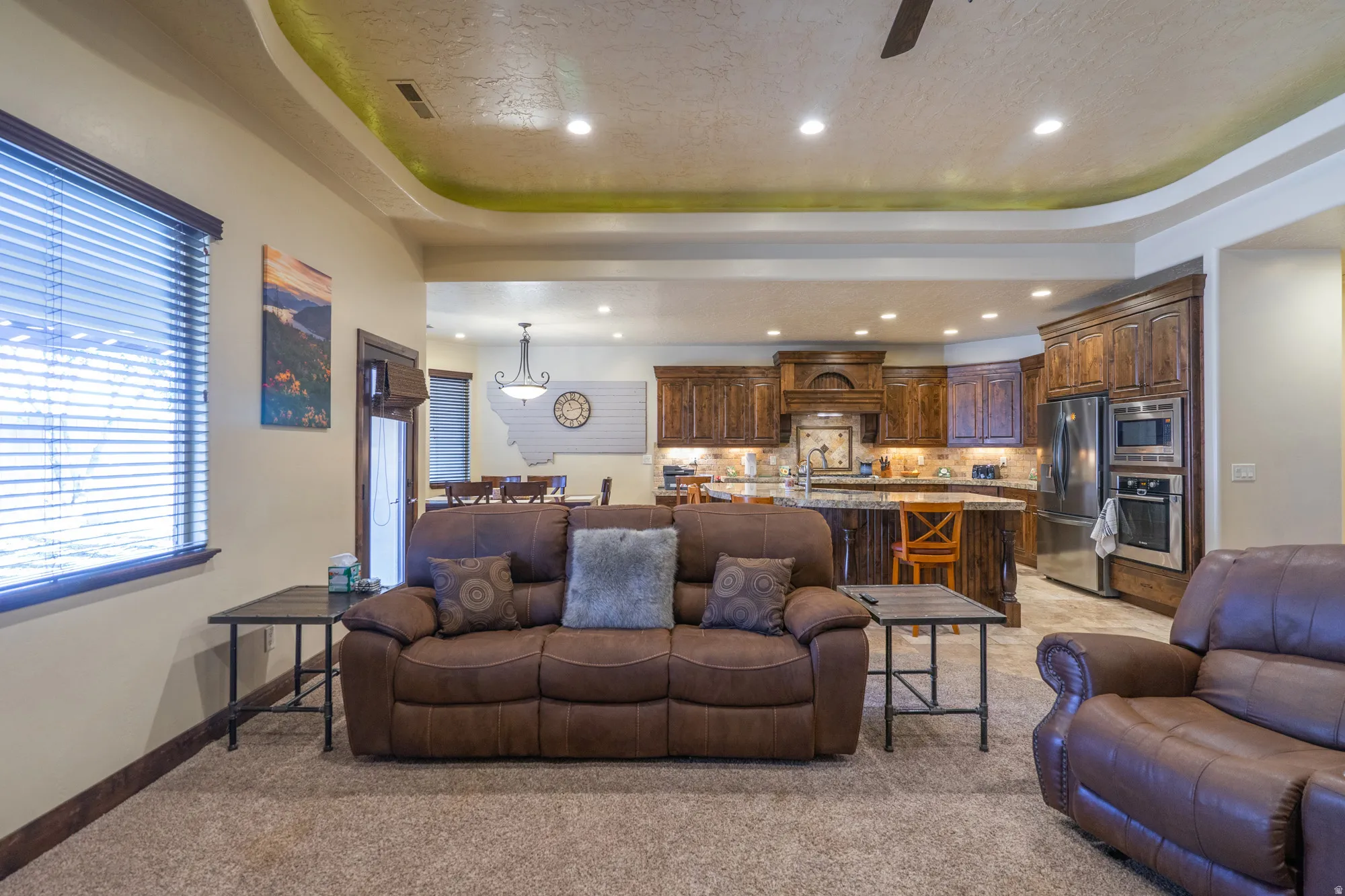 Living area with a ceiling fan, a raised ceiling, light colored carpet, and recessed lighting