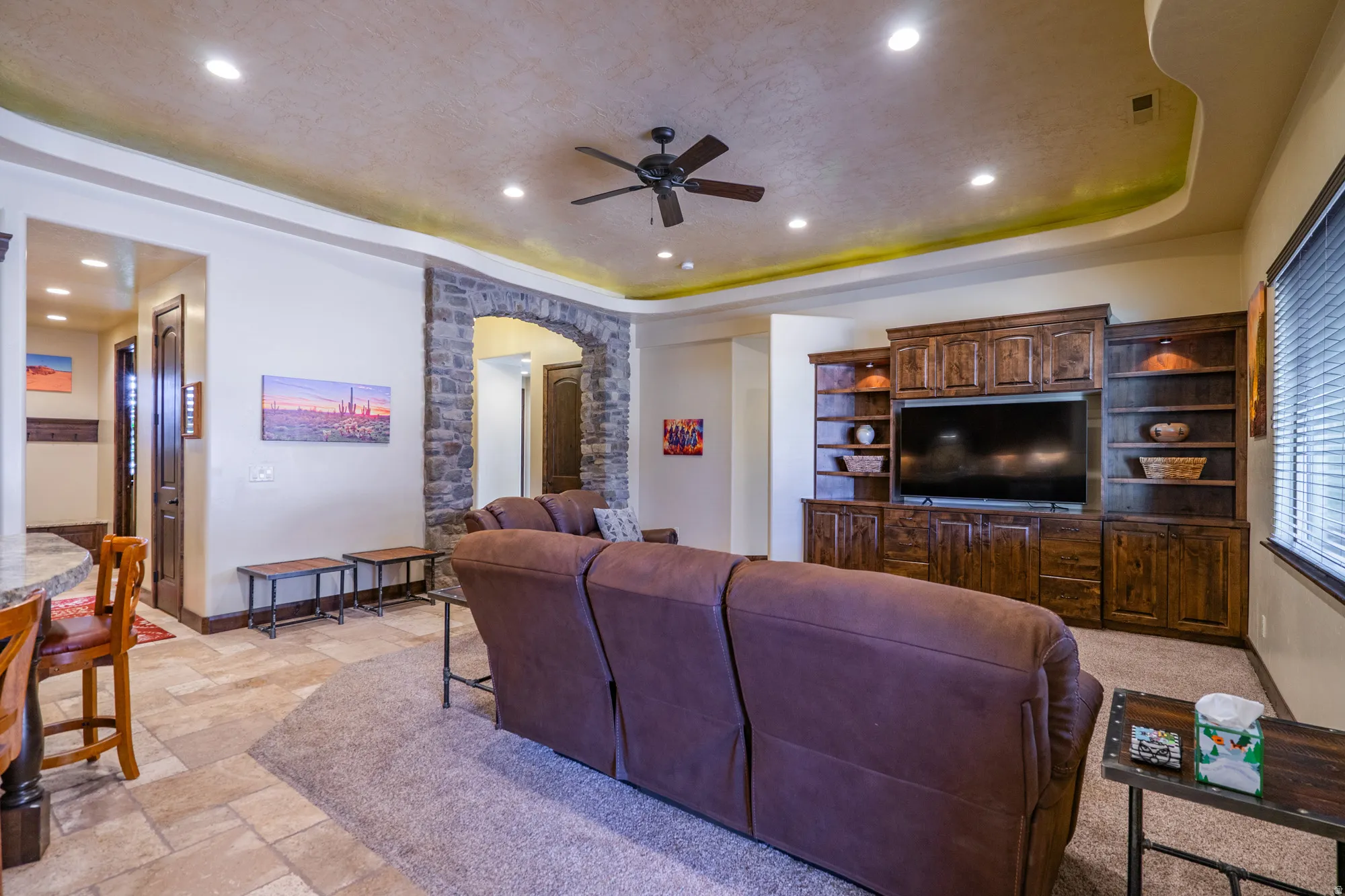Living area with arched walkways, stone tile floors, ceiling fan, recessed lighting, and a tray ceiling