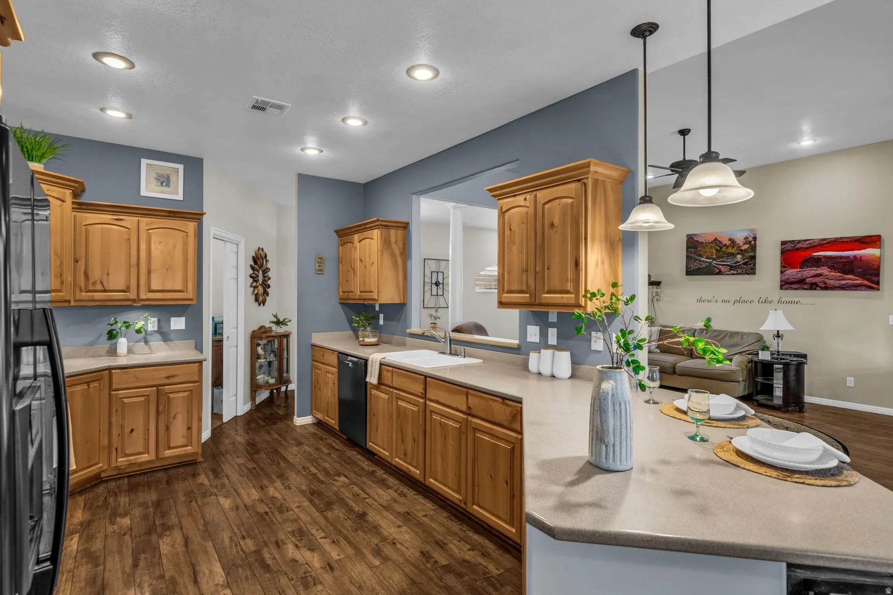 Kitchen with a peninsula, dark wood finished floors, black appliances, pendant lighting, and wood finish cabinets