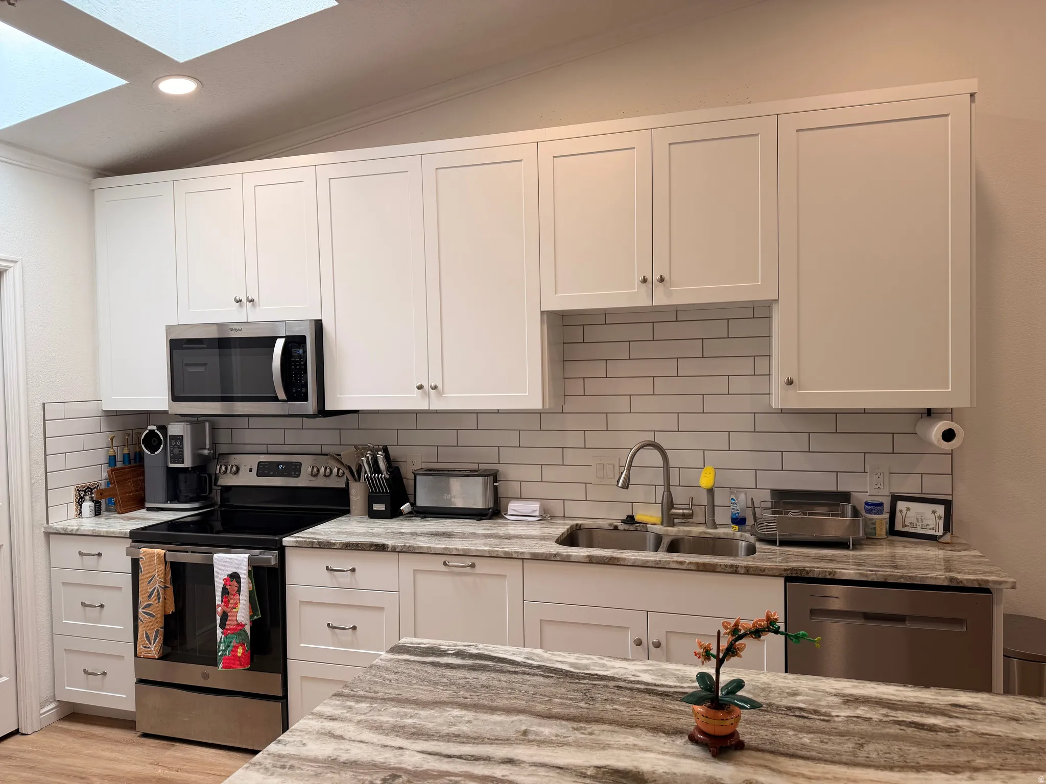 Kitchen featuring stainless steel appliances, white cabinets, light stone counters, lofted ceiling, and recessed lighting
