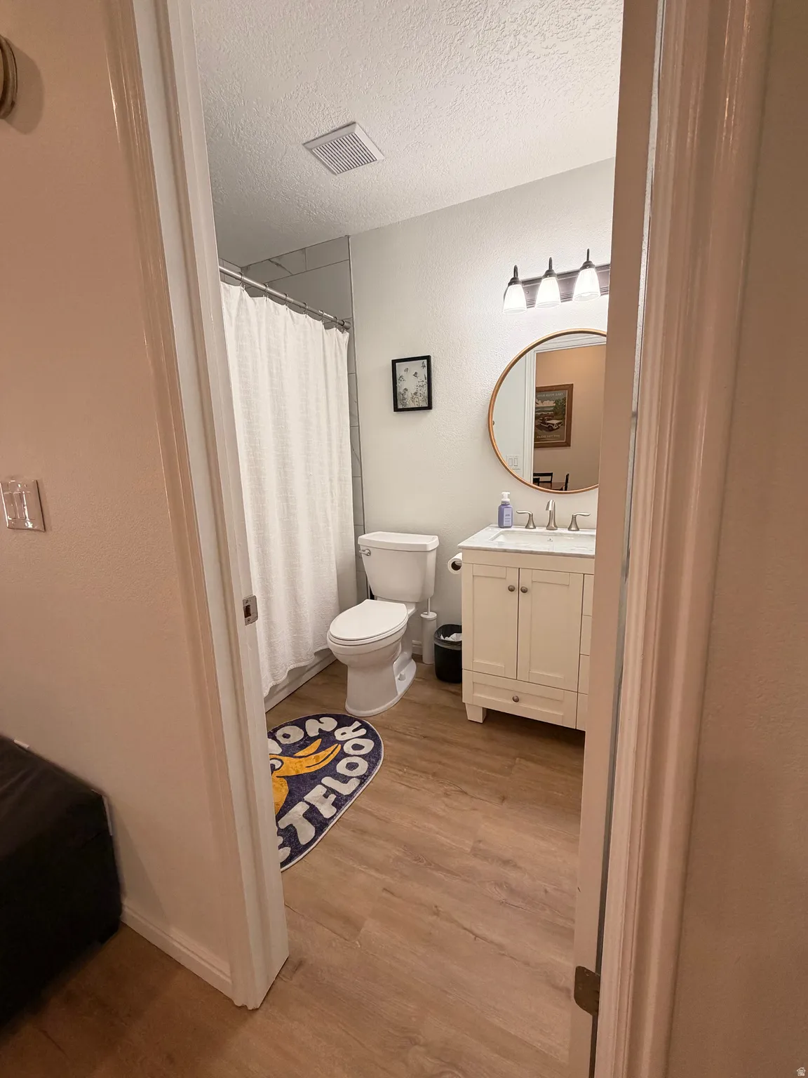 Full bath featuring vanity, light wood-style floors, a shower with shower curtain, and a textured ceiling