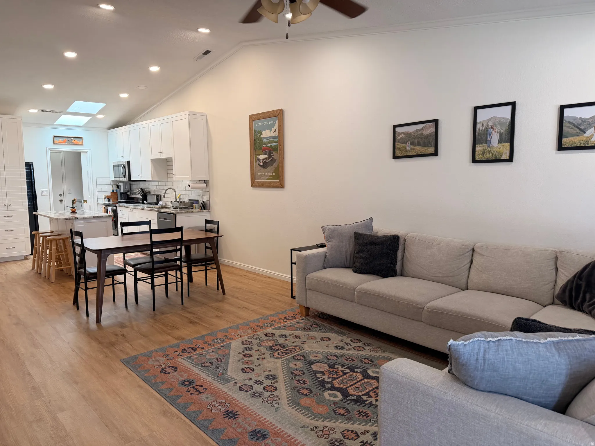 Living room featuring light wood-type flooring, vaulted ceiling, a ceiling fan, recessed lighting, and ornamental molding