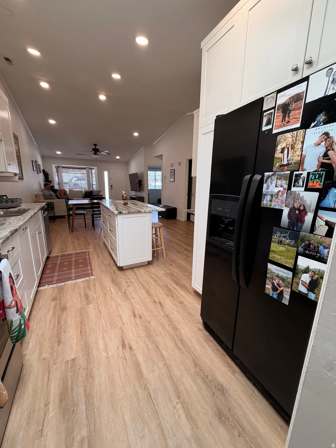 Kitchen featuring white cabinetry, a kitchen bar, black fridge with ice dispenser, light wood finished floors, and light stone countertops