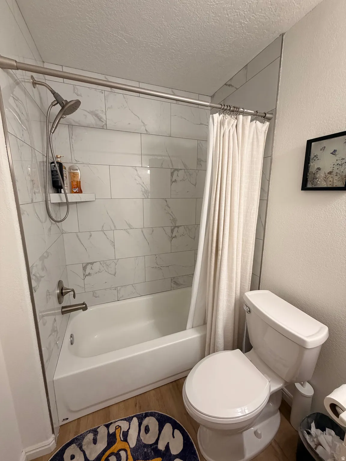 Full bath with a textured wall, a textured ceiling, wood finished floors, and shower / bath combo