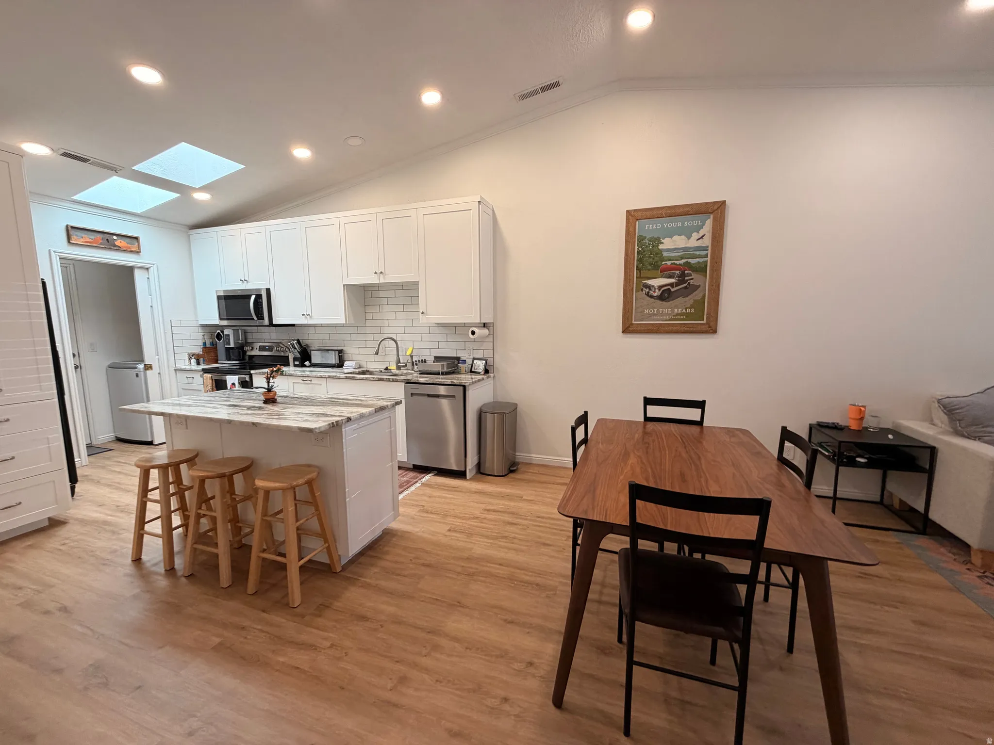 Kitchen with lofted ceiling, white cabinets, recessed lighting, light stone counters, and a kitchen breakfast bar
