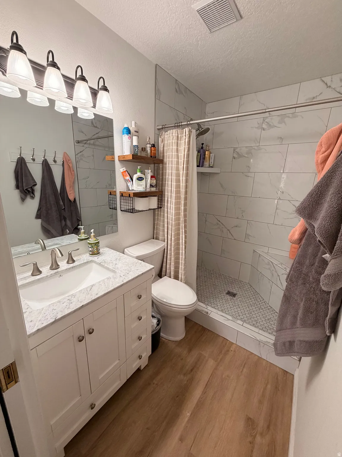 Full bath with vanity, a shower stall, light wood-type flooring, and a textured ceiling