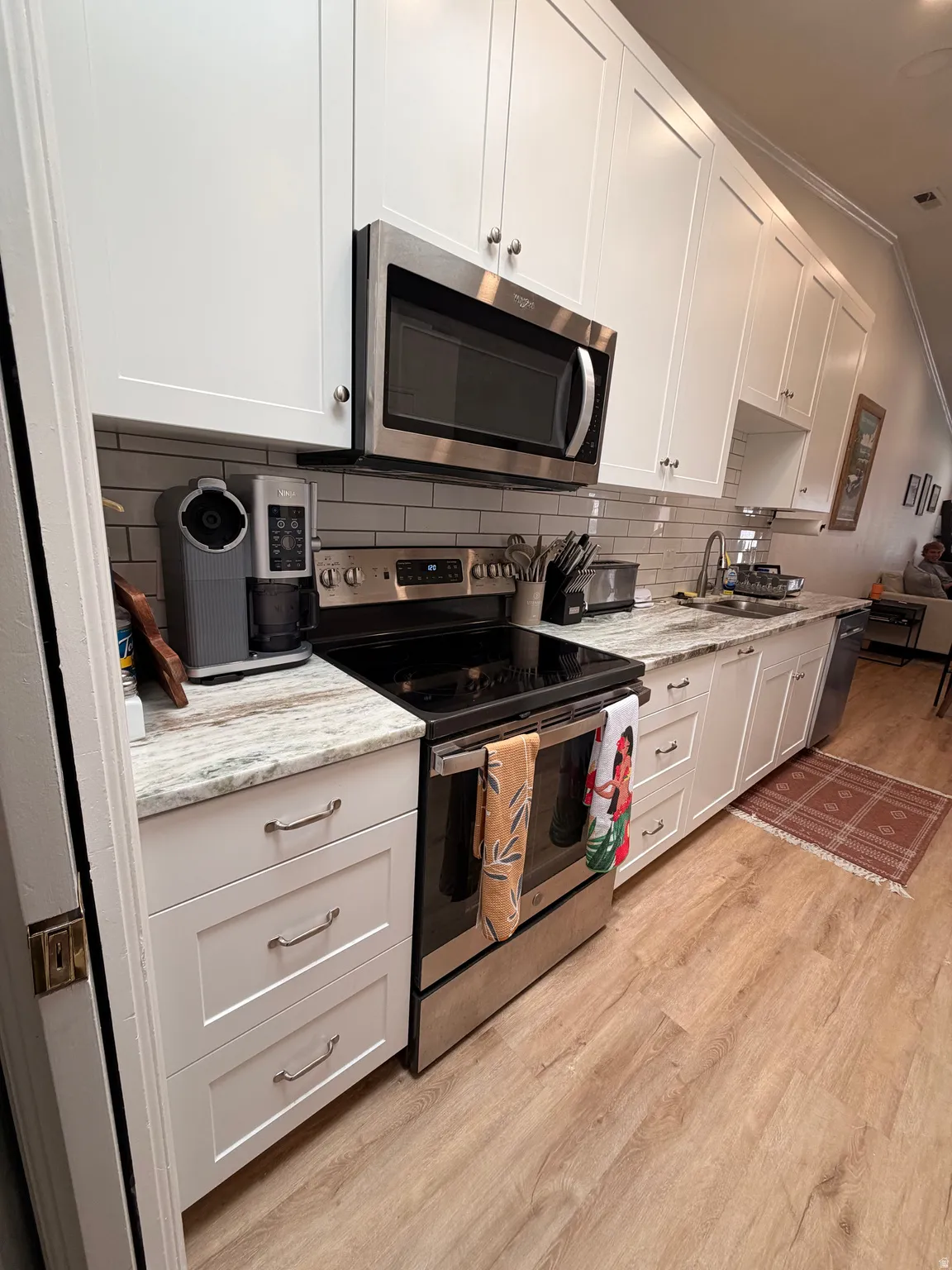 Kitchen with stainless steel appliances, ornamental molding, white cabinetry, light wood-style floors, and light stone countertops