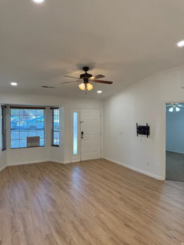 Wood-finish flooring, recessed lighting, ceiling fan light fixture, white front door with frosted glass sidelight, and bay windows with blinds