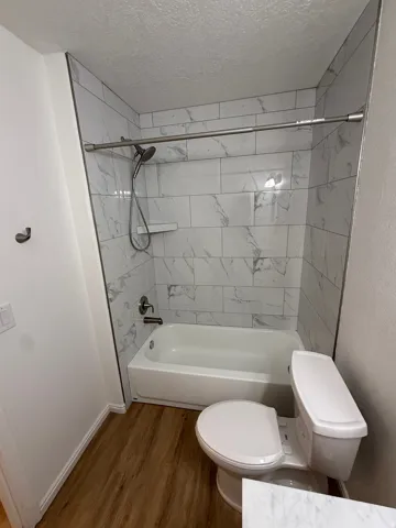 Bathtub with white subway tile surround, brushed nickel shower fixtures, and wood-finish flooring
