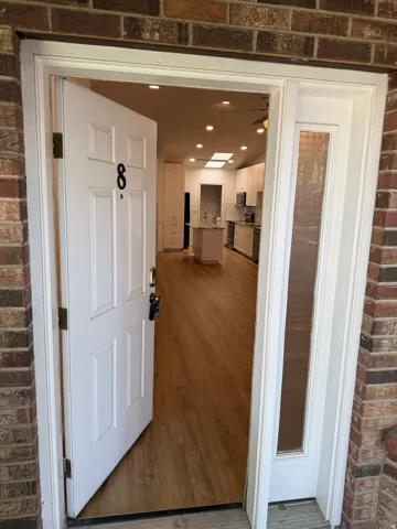Brick exterior with a white entry door, frosted sidelight, wood-finish flooring, recessed lighting, and a skylight