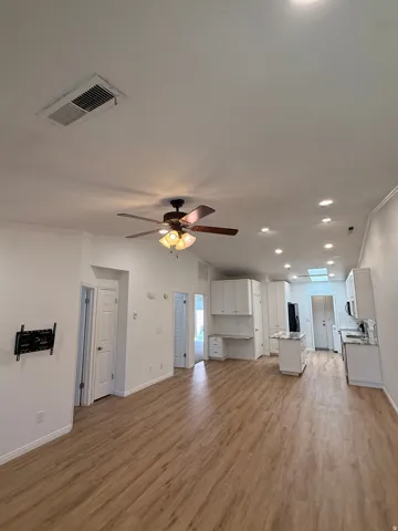 Expansive room featuring wood-finish flooring, recessed lighting, a ceiling fan, white cabinetry with countertops, and a skylight