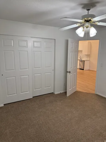 Brown carpet flooring, white paneled doors, and a ceiling fan with integrated lighting