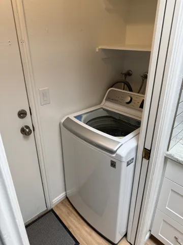 Dedicated laundry area featuring wood-finish flooring, a white built-in shelf, and a white interior door